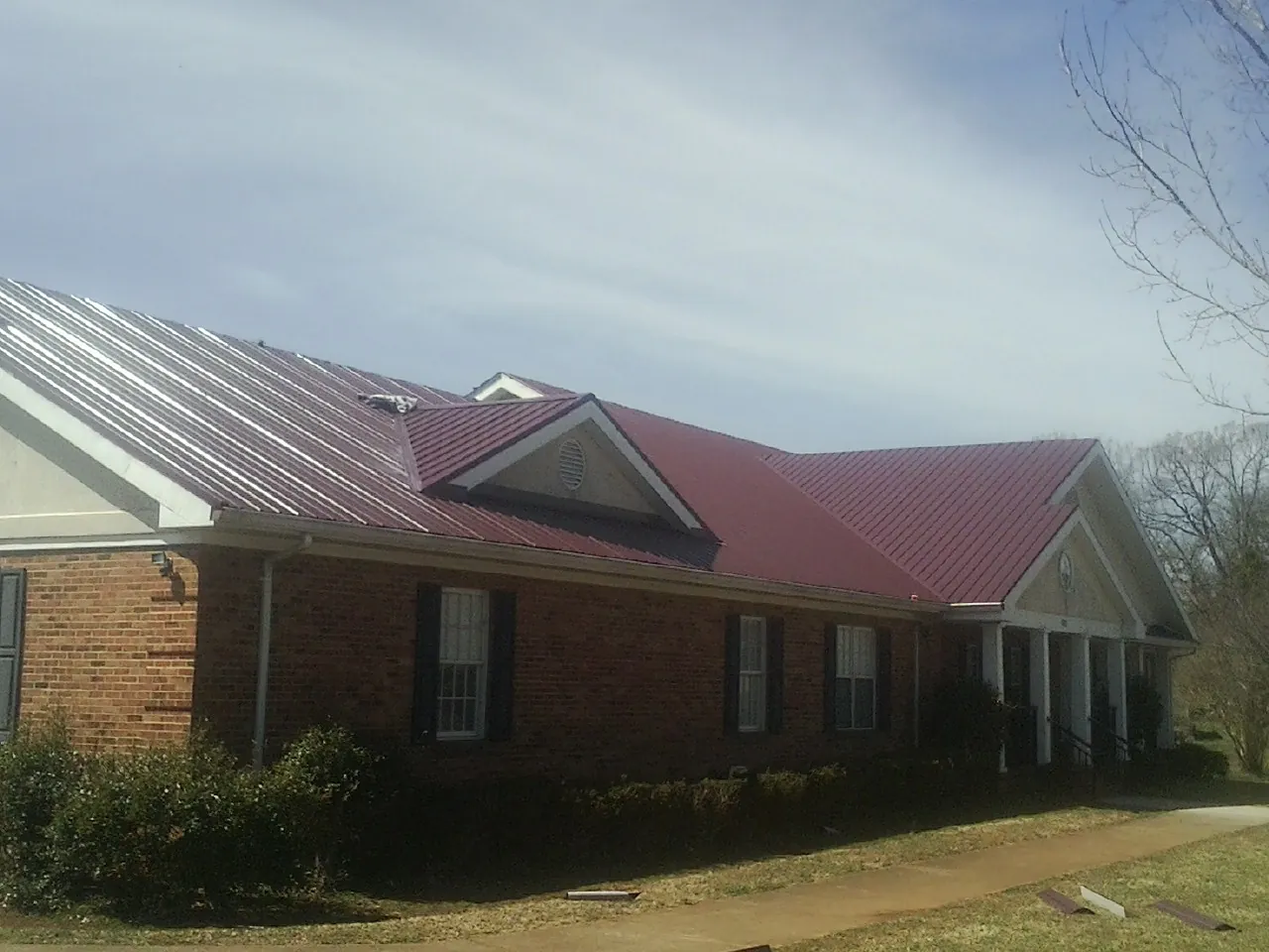 Red metal roof with gabled entries on a long brick building, from a Hail Damage Roof Repair job in Wrightsville Beach