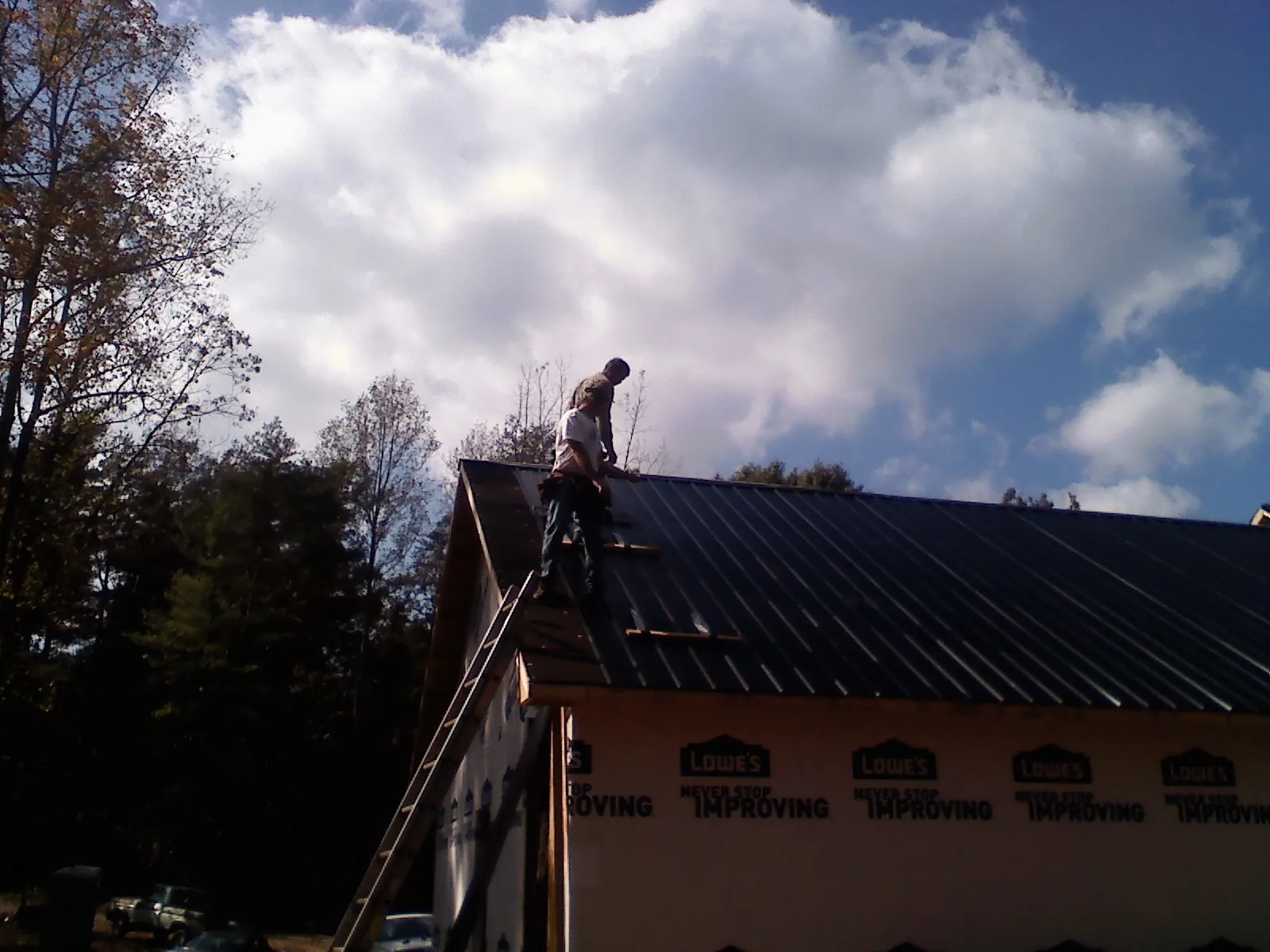 Roofer fastening dark metal panels high against a cloudy sky, from a Roof Inspection job in Wrightsville Beach