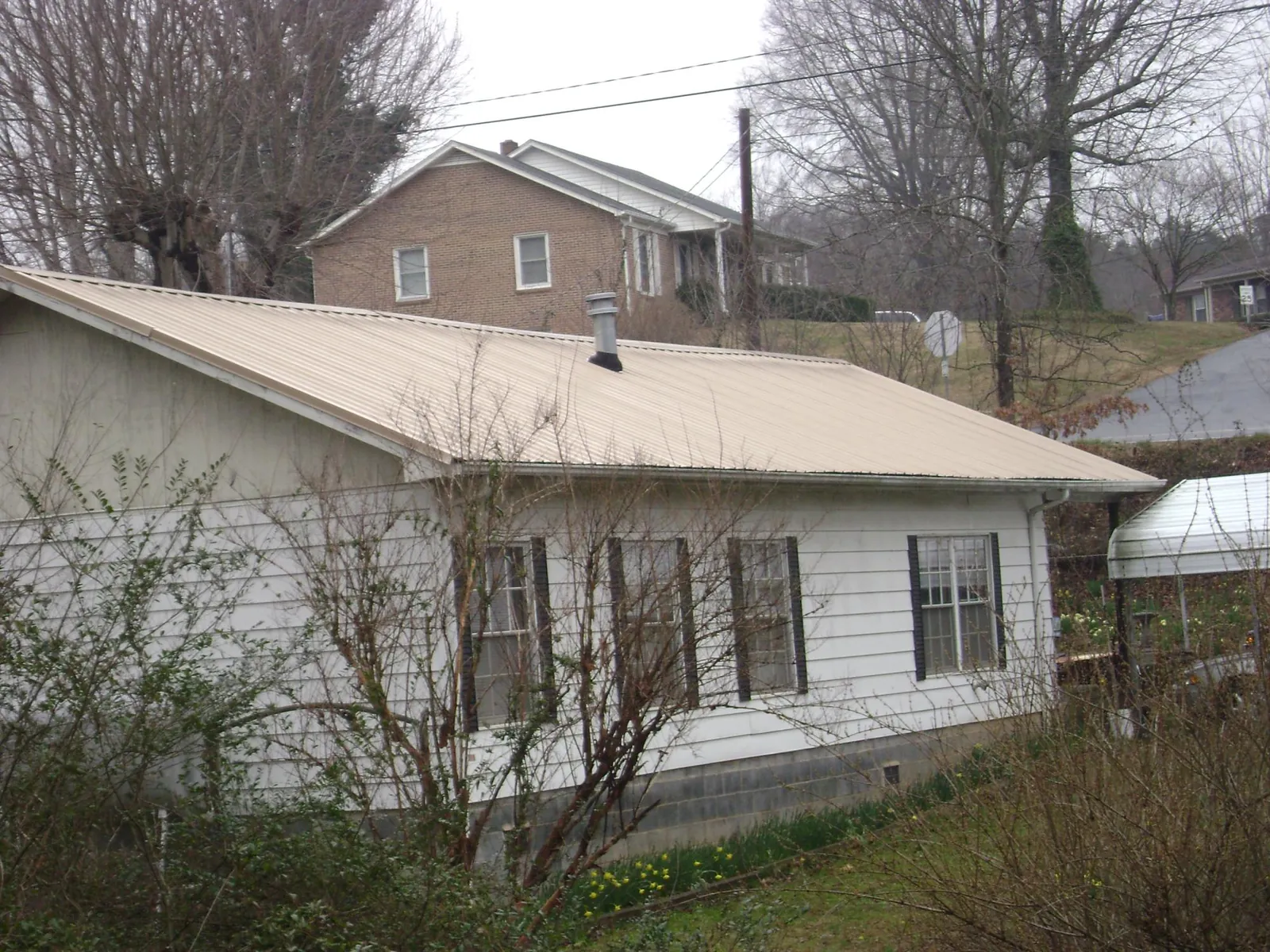 Tan metal roof on a white sided house set into a hillside — Commercial Roofing by Roofing Brothers in Wrightsville Beach